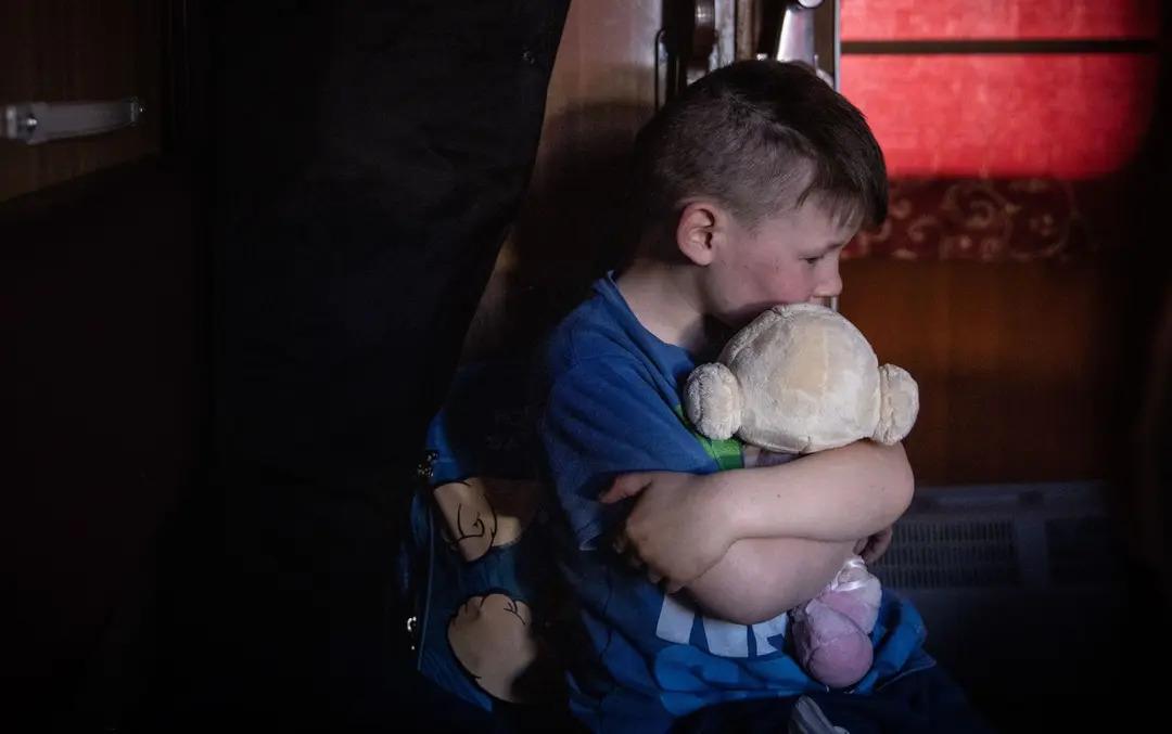 A boy on a train hugs a soft toy during an evacuation from Polohy, Zaporizhzhia Oblast, Ukraine, to western Ukraine on Spring 2022